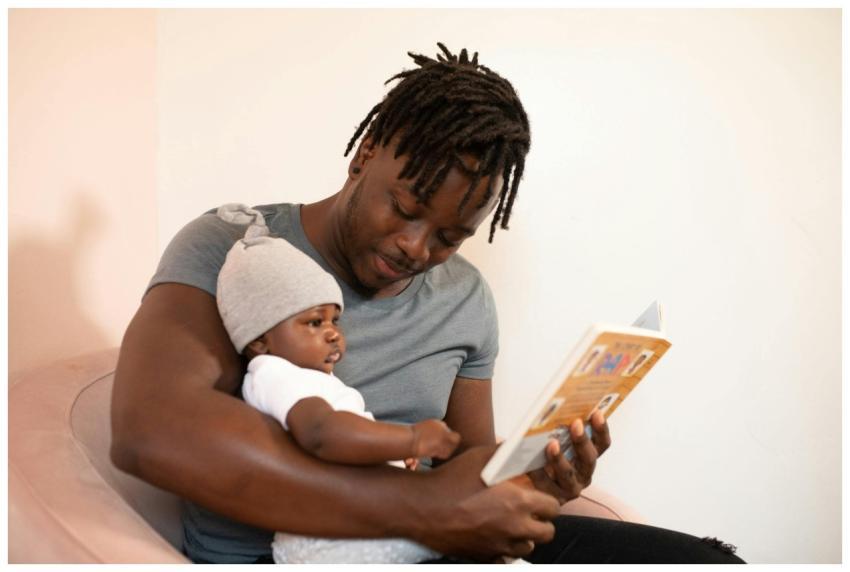 A father with dreadlocks reads a book to his baby,