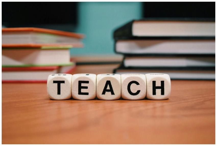 Close-up of dice spelling 'TEACH' amidst stacked b