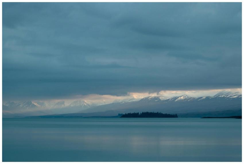 Calm lake with snow-capped mountains under a cloud