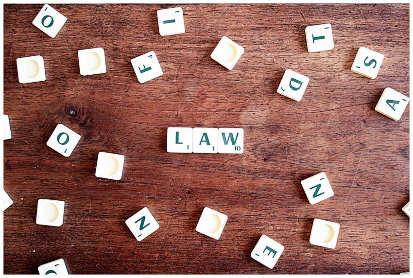 Scrabble tiles spelling 'LAW' on a wooden table, s