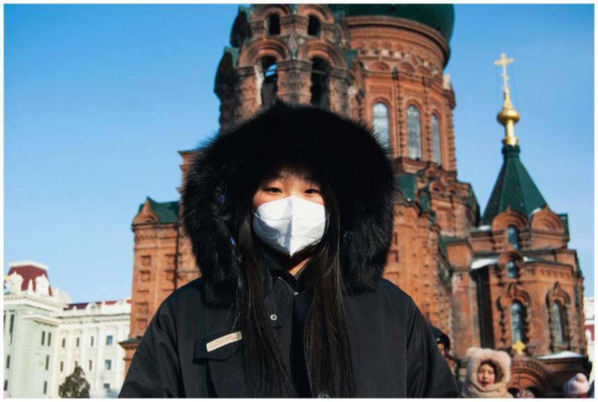 Woman in a winter coat and mask stands before the