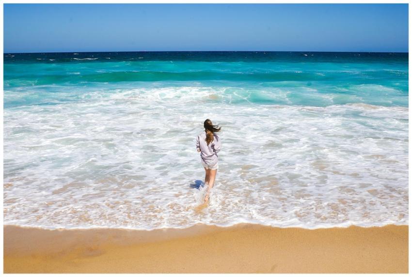 A woman stands on a sandy beach, gazing at the tur