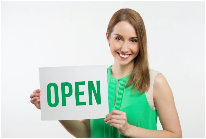 Cheerful woman in green holding an open sign, perf