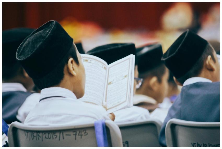 Boys in traditional attire reading the Quran durin