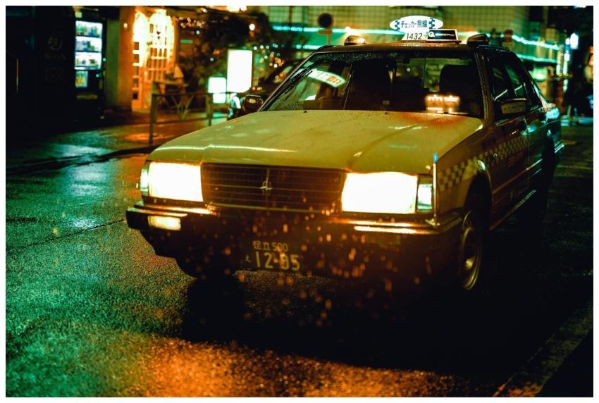 A yellow taxi driving through rainy streets at nig