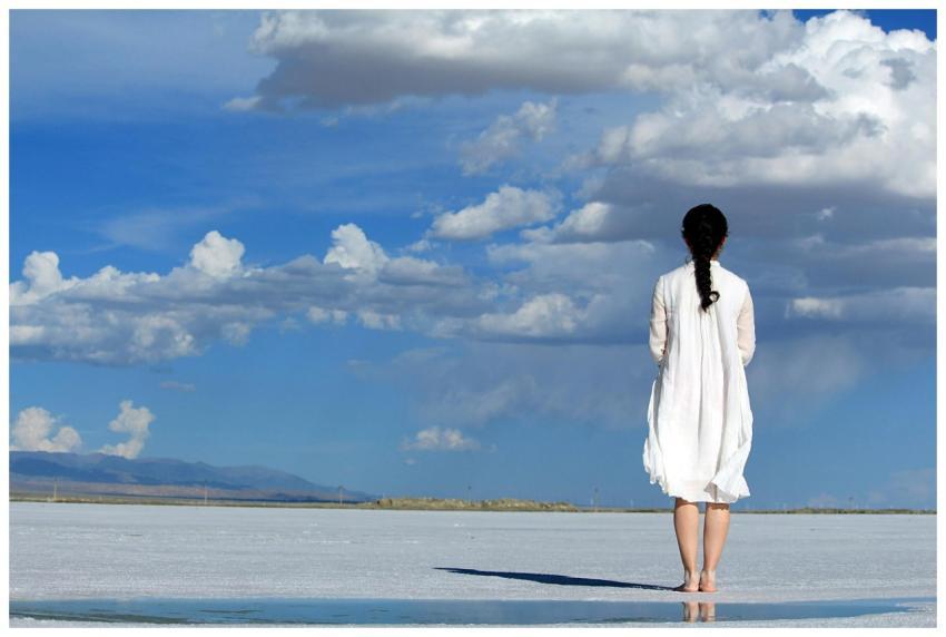 Woman stands alone on a vast salt flat under a bri