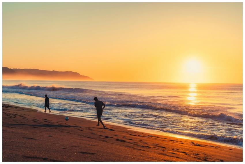 Two individuals playing soccer on a sandy beach du