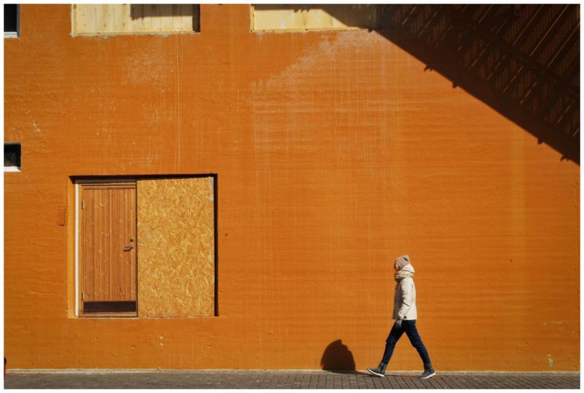 A person walks along a vibrant orange wall, castin