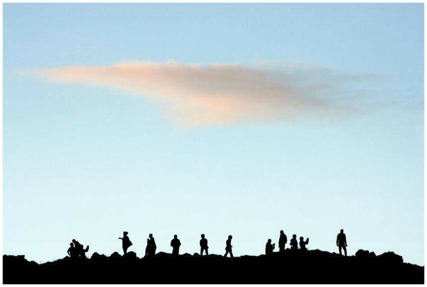 A silhouette of people gathered on a hill with a c