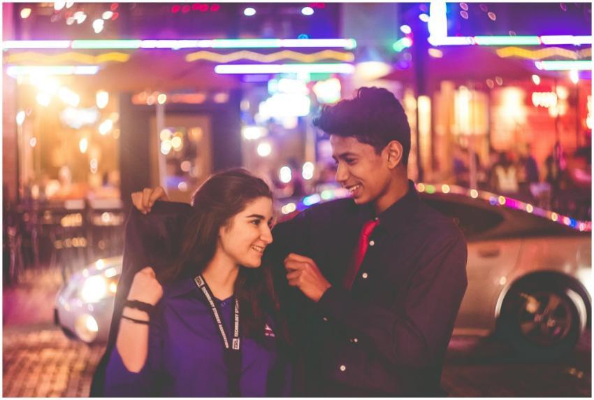 A young couple smiles warmly under vibrant city li