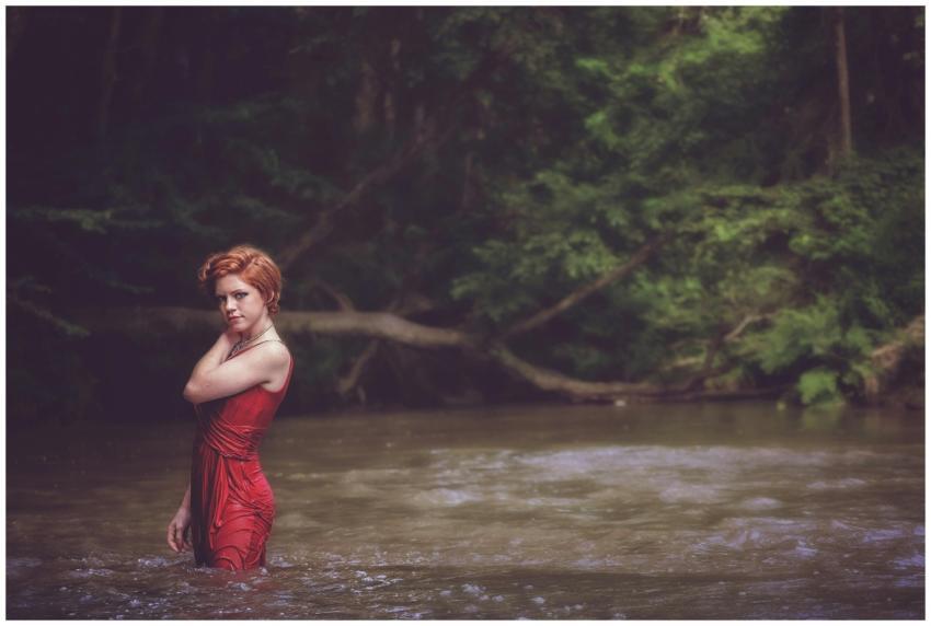 A stylish redhead woman stands elegantly in a rive