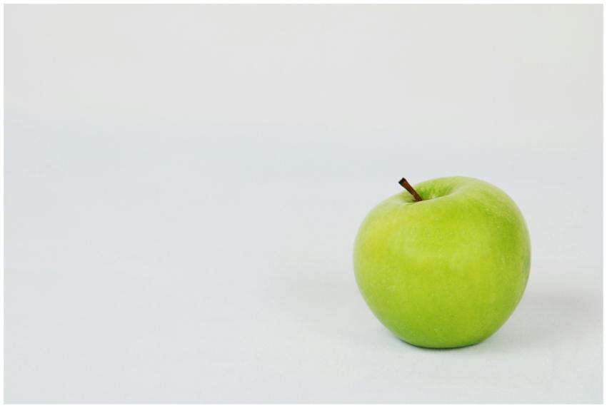 A single green apple placed against a crisp white