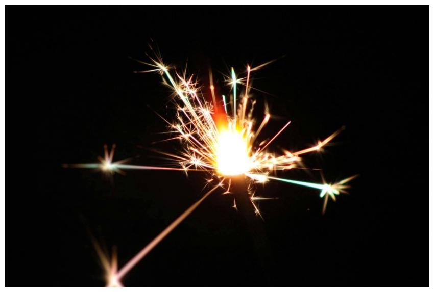 A vibrant sparkler bursts with light against a dar