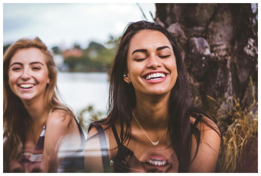 Two women happily laughing together outdoors by a