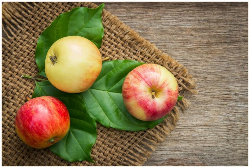 Three ripe apples on leaves over a rustic wooden b