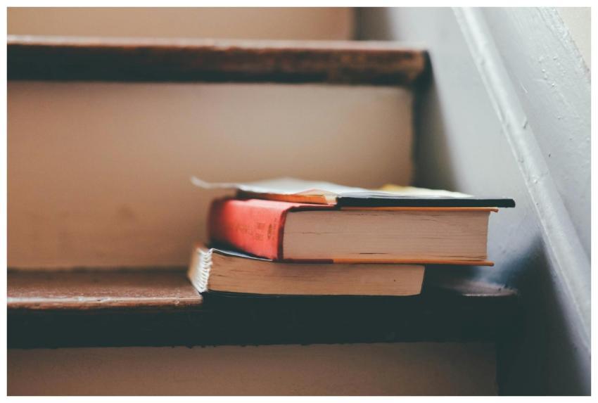 A small pile of books rests on wooden stairs, symb