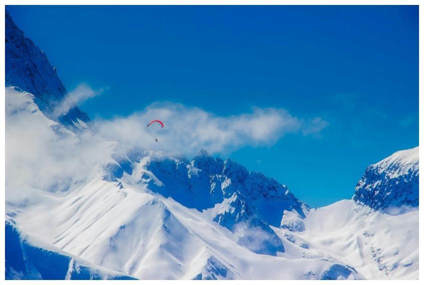 A paraglider soars above pristine snow-covered pea