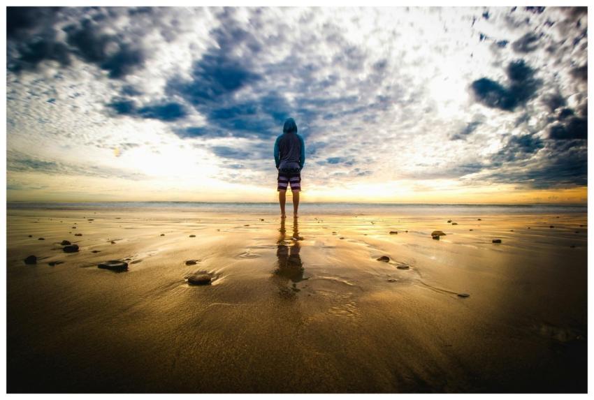 A lone figure stands on a tranquil beach during a