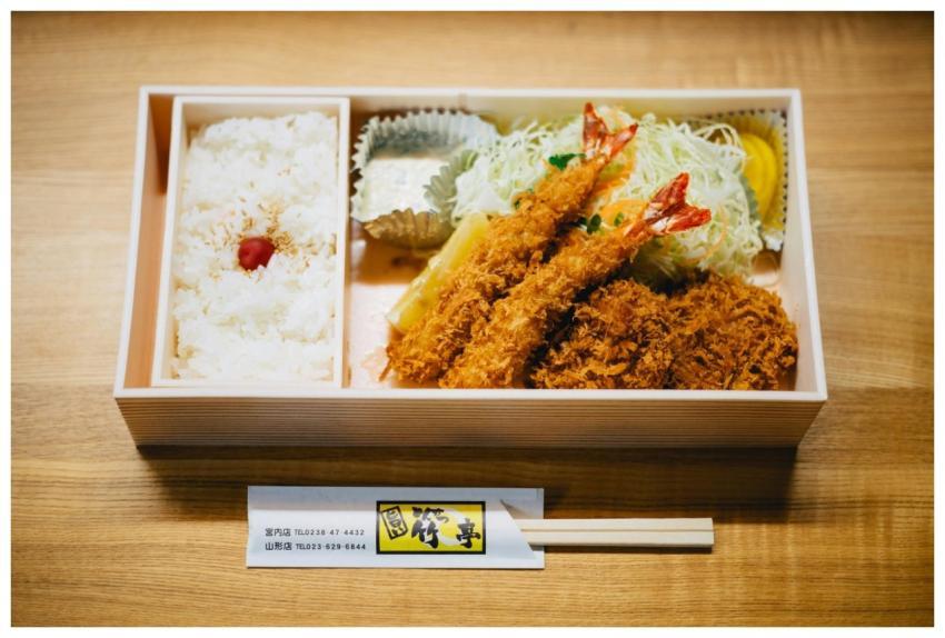 A Japanese bento box featuring rice, prawns, and s