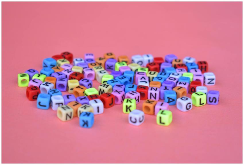 Vibrant alphabet cube beads scattered on a pink ba