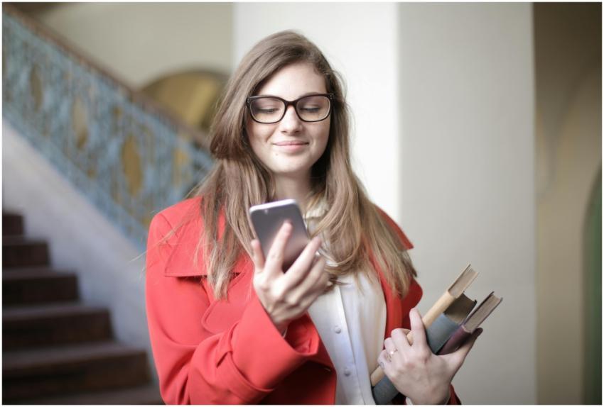 Happy female student in red coat holding smartphon