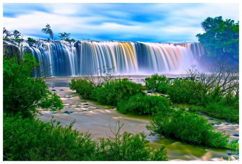 Vibrant waterfall amidst lush greenery under a cle