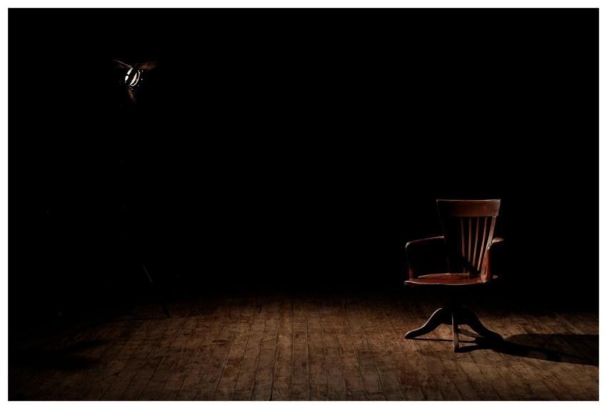 A vintage wooden chair is spotlighted in a dark st