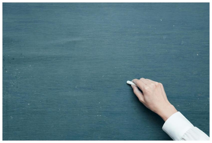 Hand holding chalk ready to write on a blank black