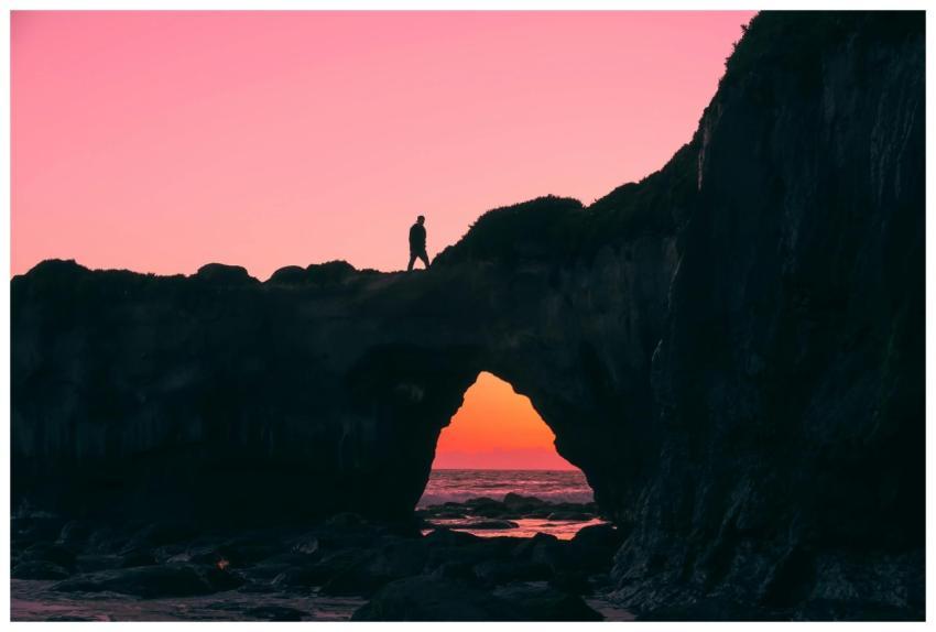 A person silhouetted on a coastal rock arch after