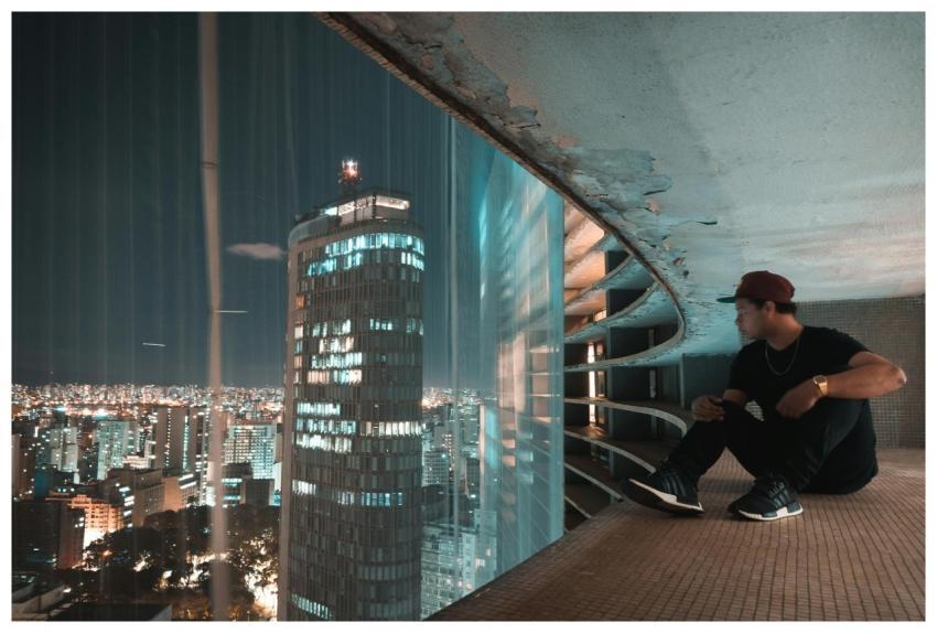 A man sits on a rooftop, overlooking illuminated s