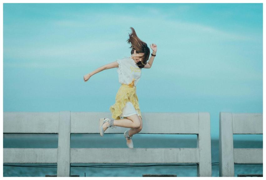 Woman jumping cheerfully on a bridge under a sunny