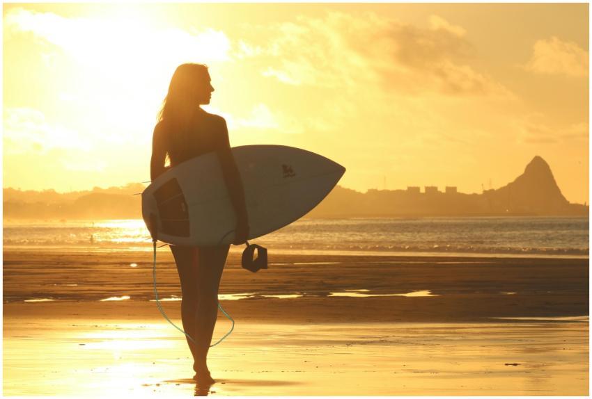 A silhouette of a woman holding a surfboard, stand