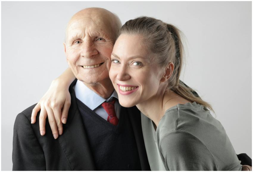 Cheerful elderly man and adult woman cuddling on w