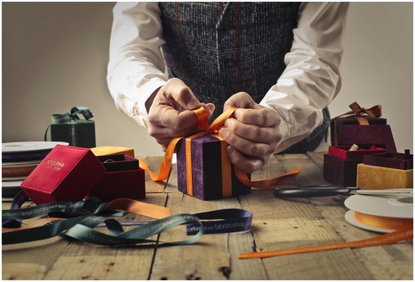 A person wraps a gift with orange ribbon on a rust
