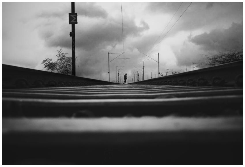 A solitary figure walks on railway tracks under a