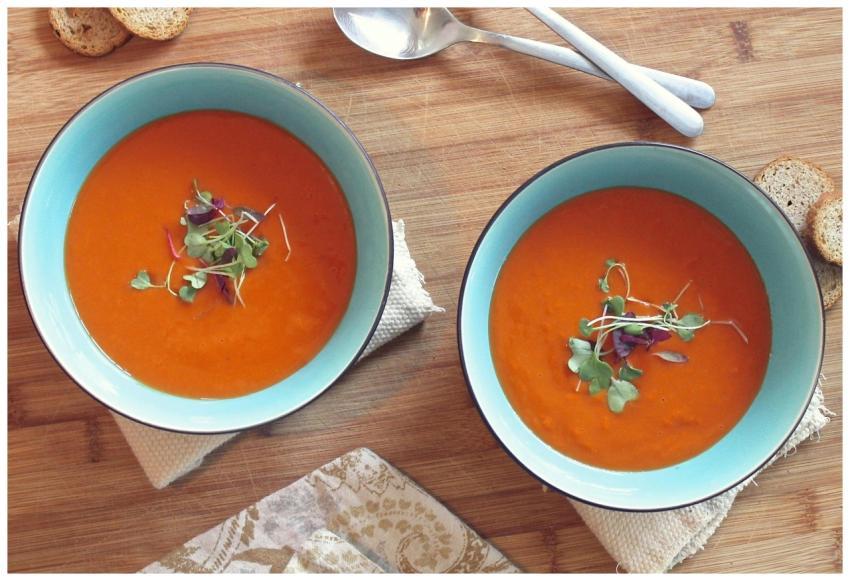 Two bowls of vibrant tomato soup garnished with fr