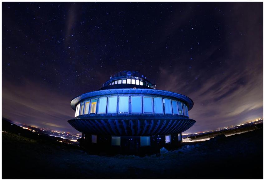 A UFO-shaped building lit up under a vibrant starr