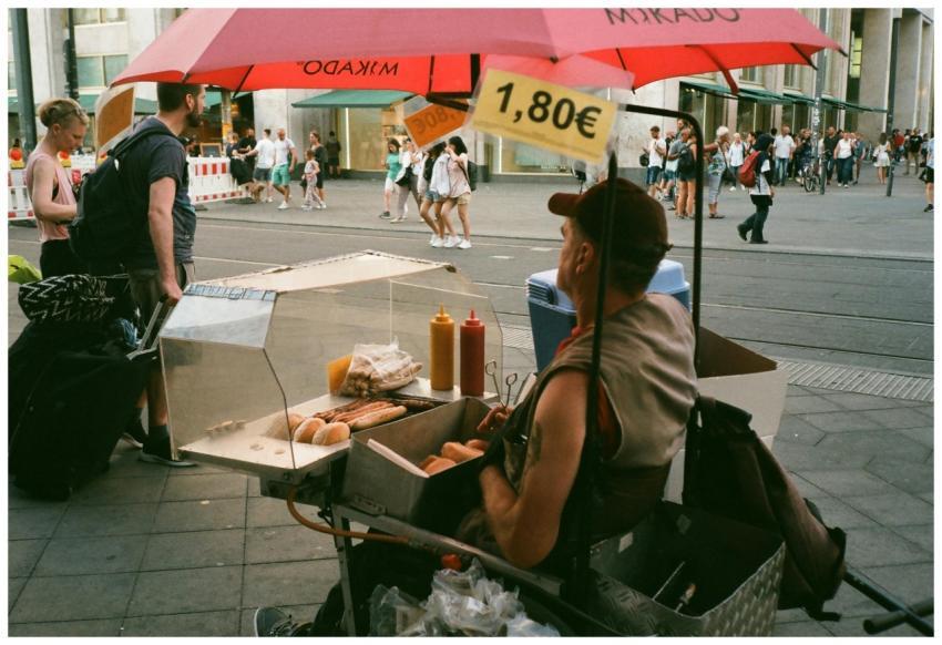 A street vendor sells hotdogs under a red umbrella