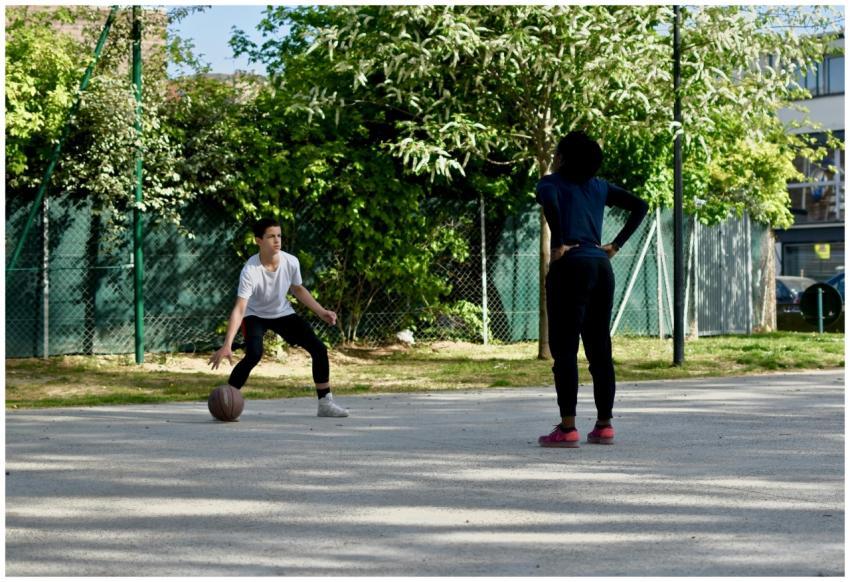 Two people playing basketball outdoors in a sunny