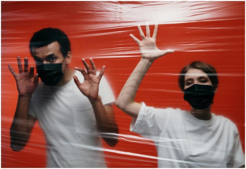 Two people wearing masks stand behind a plastic fi