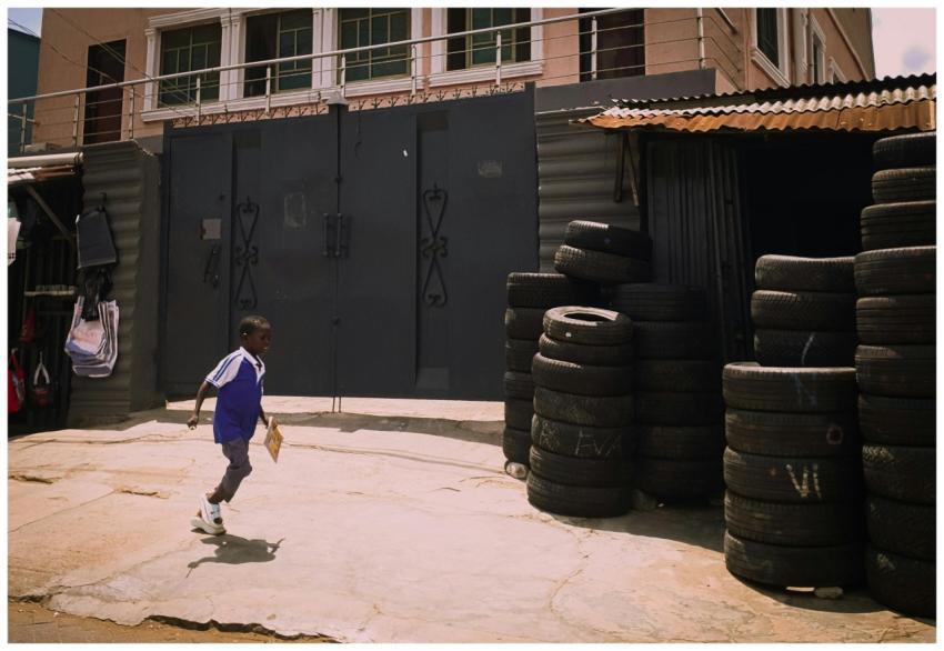 A young boy runs past a roadside tire shop in an u