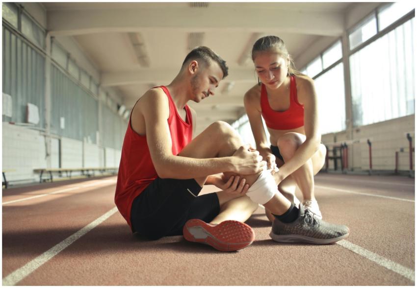 A woman helps an injured man's leg on an indoor tr