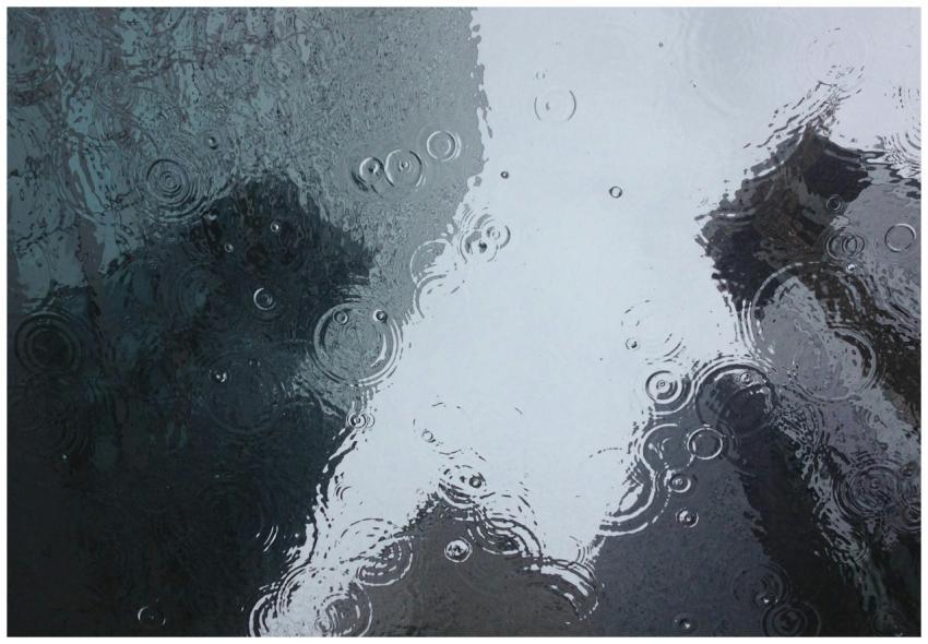 Raindrops create ripples on a window, reflecting a
