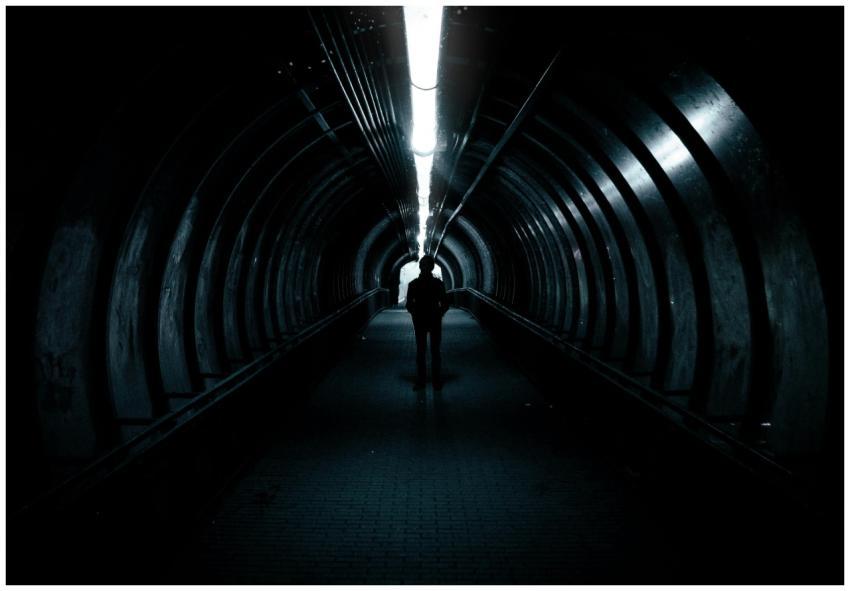 A lone figure stands in a dimly lit tunnel, creati