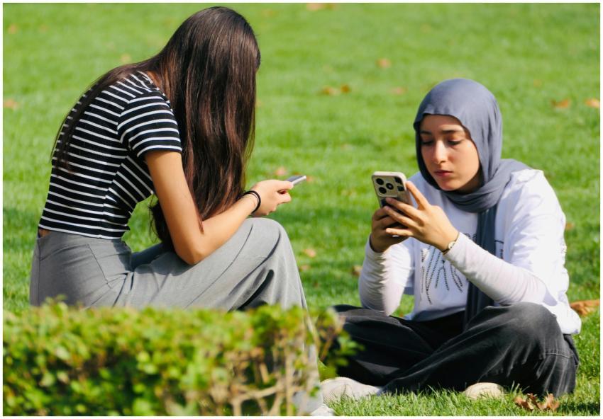 Two young women sit on grass, focused on their sma