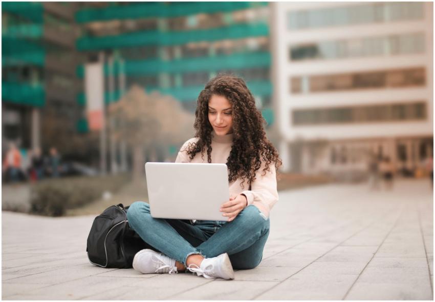 A woman with curly hair using a laptop while sitti