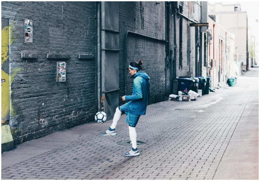 A man practicing soccer in a gritty urban alleyway