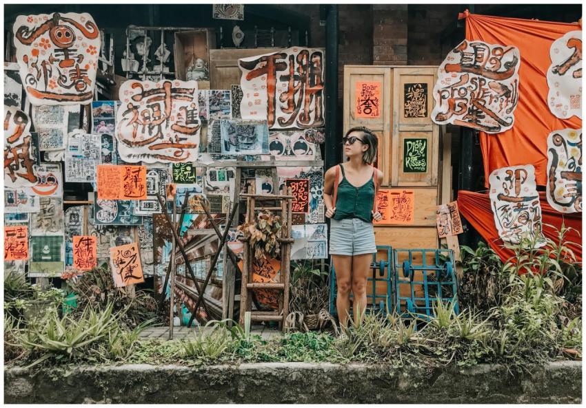 A young woman stands in front of an artistic wall
