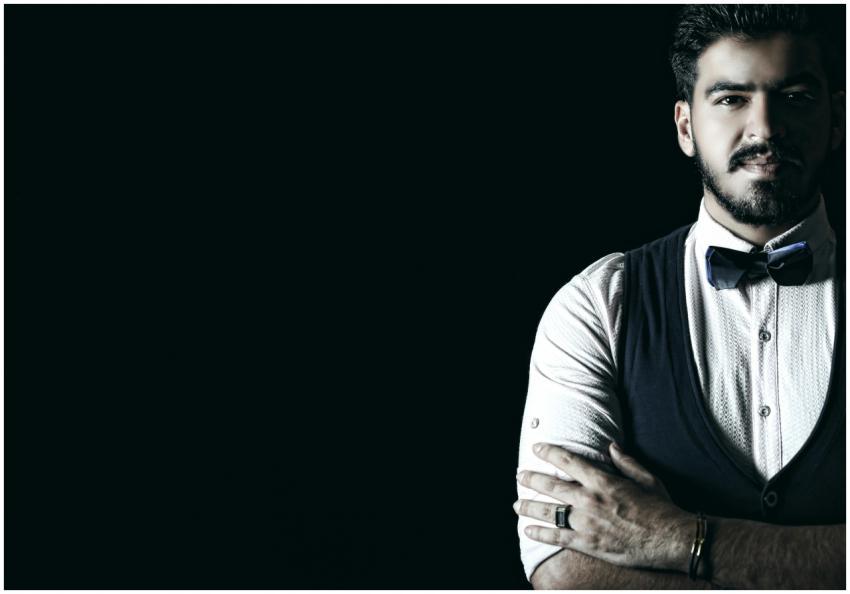 A stylish man wearing a bow tie and vest, posing c