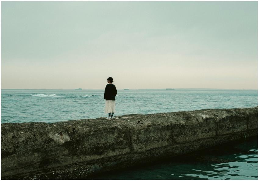 A contemplative woman stands on a pier, looking ou